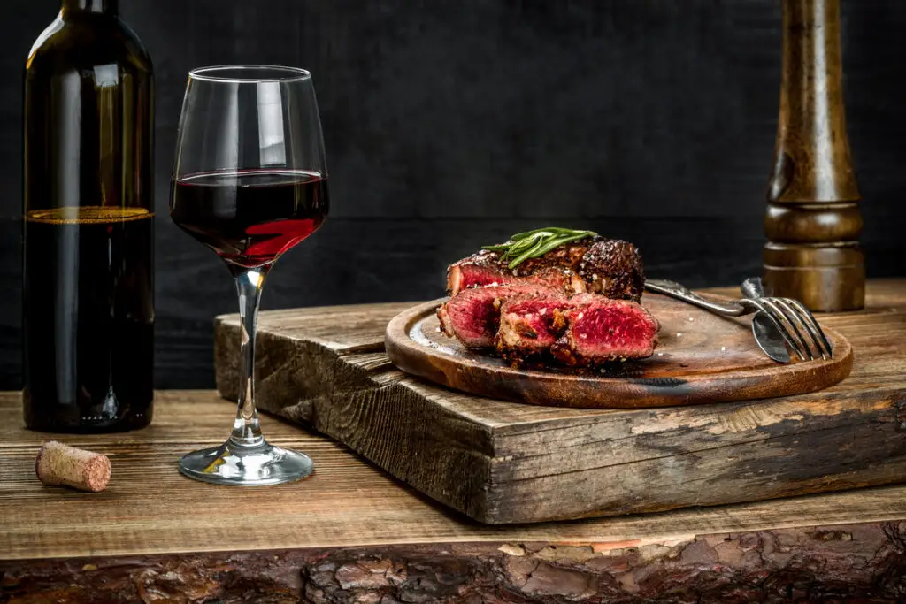 Grilled ribeye beef steak with red wine, herbs and spices on wooden table