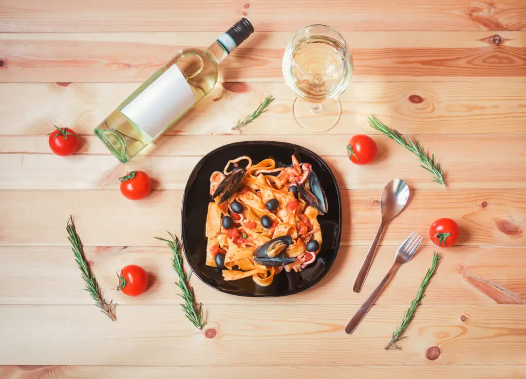 Pappardelle pasta with seafood with tomato sauce, glass of white wine and bottle of white wine. Top view.