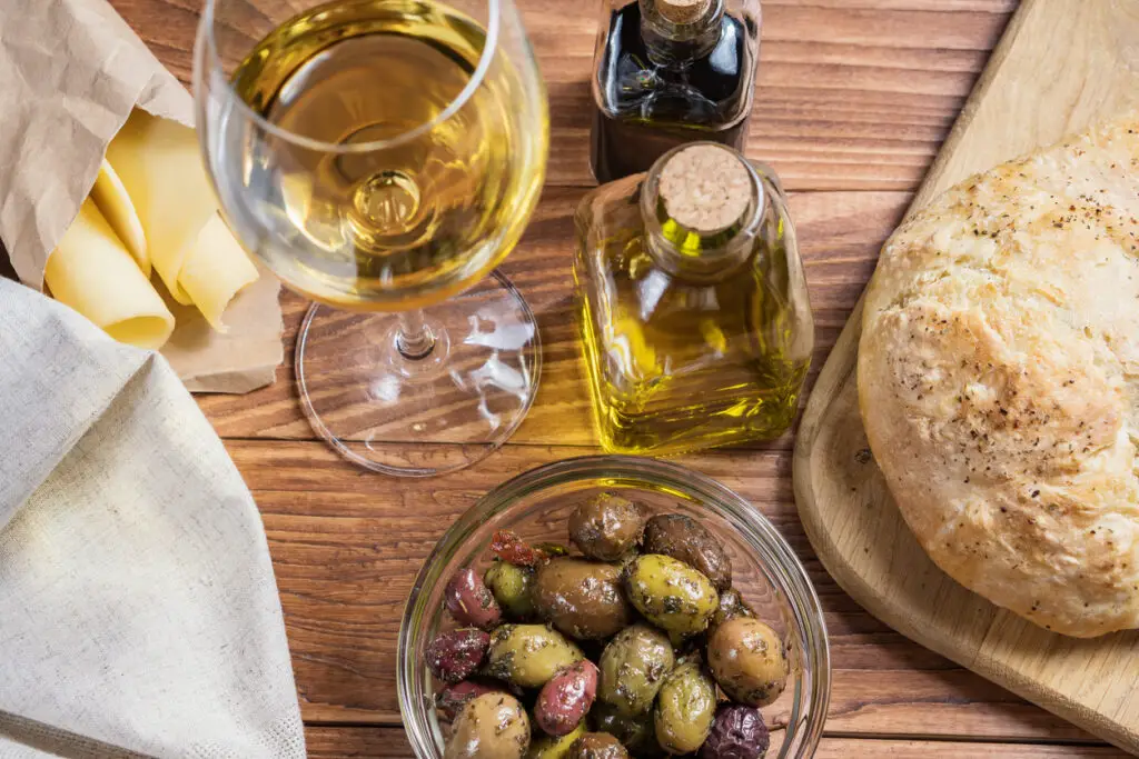 Bowl with different kind of olives, glass of wine, cheese and  fresh bread ciabatta on the wooden table.