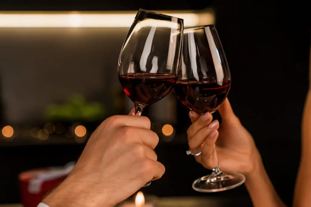 Close up shot of man and woman toasting and drinking red wine from glasses on dinner