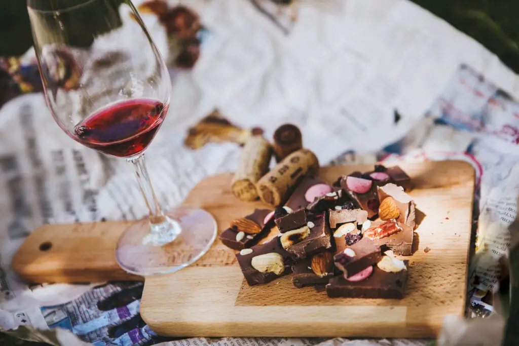 Glass with red wine and pieces of chocolate with nuts and raisins