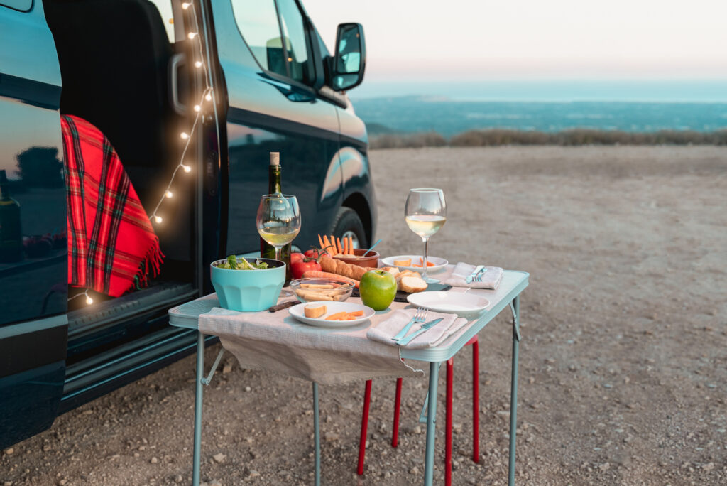 Healthy vegan picnic celebration in camper van with landscape in background - Focus on food
