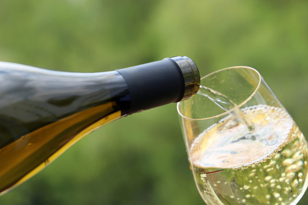White wine pouring from the bottle into the glass on green nature blurred background