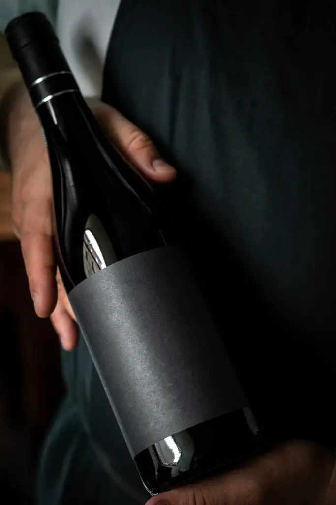 A full Bottle of wine in the hands of a male sommelier with a black label. Mock-up for red wine design.