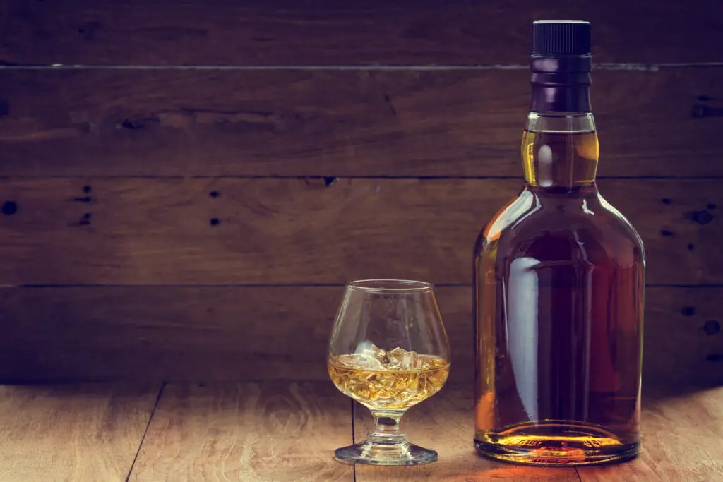 bottle and glass of whiskey on a wooden background made with vintage tones