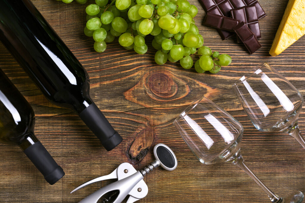 Bottles and glasses of wine, cheese and ripe grapes on wooden background
