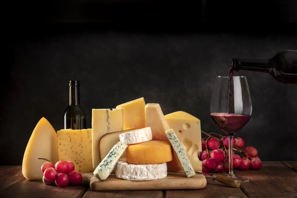 Cheeses with grapes and pouring wine, a side view on a dark background with copy space
