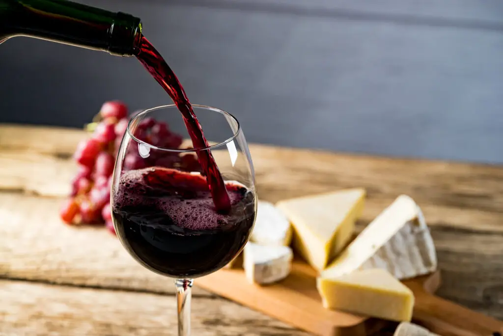 Pouring red wine into the glass against wooden background