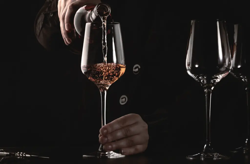 Sommelier pouring rose wine into glass at wine tasting in winery, bar or restaurant. Dark background