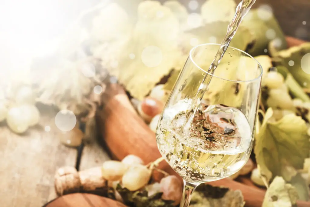 White wine being poured into a glass, vintage wood background, selective focus