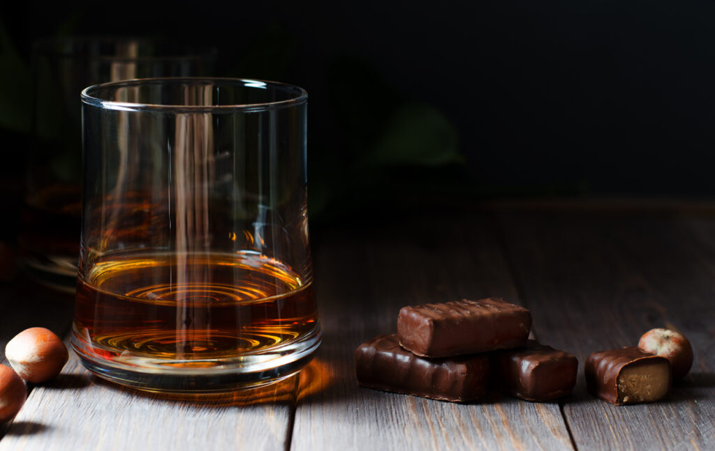 Cognac or whisky or brandy in a glass. Pieces of chocolate and hazelnuts. Dark background. Copy space