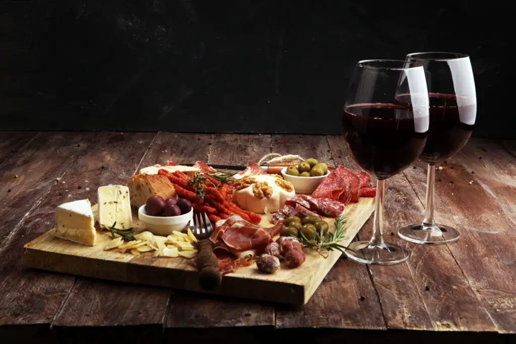 Cutting board with prosciutto, salami, cheese,bread and olives on dark wooden background