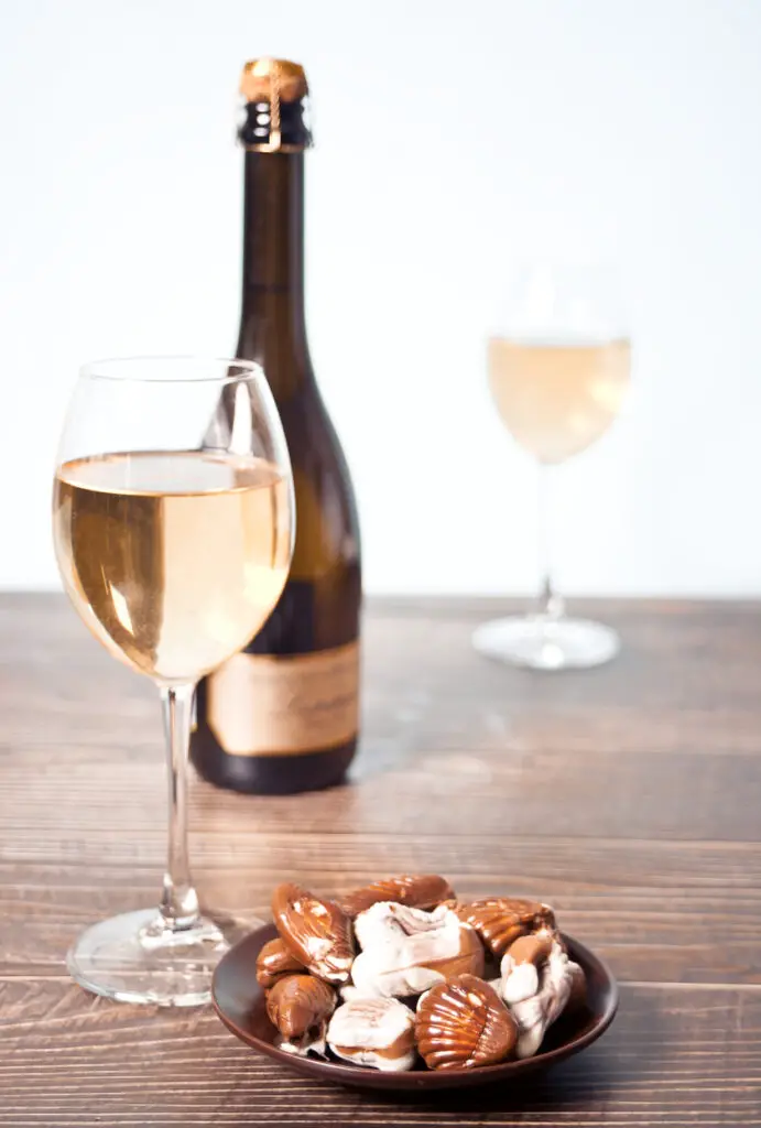 Glasses of champagne or white grape wine with plate of chocolates, bottle on the background