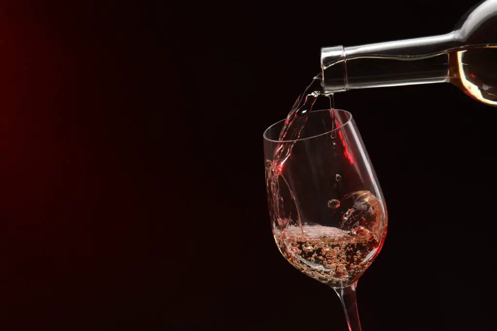 Pouring white wine from bottle into glass on dark background, space for text