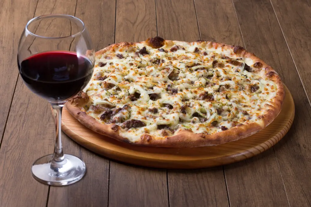 Meat pizza on wooden board. Made with Mozzarella, picanha meat, onion, cheese, tomato sauce. Filet Steak, meat. Glass of red wine to accompany. Gastronomic Photo.