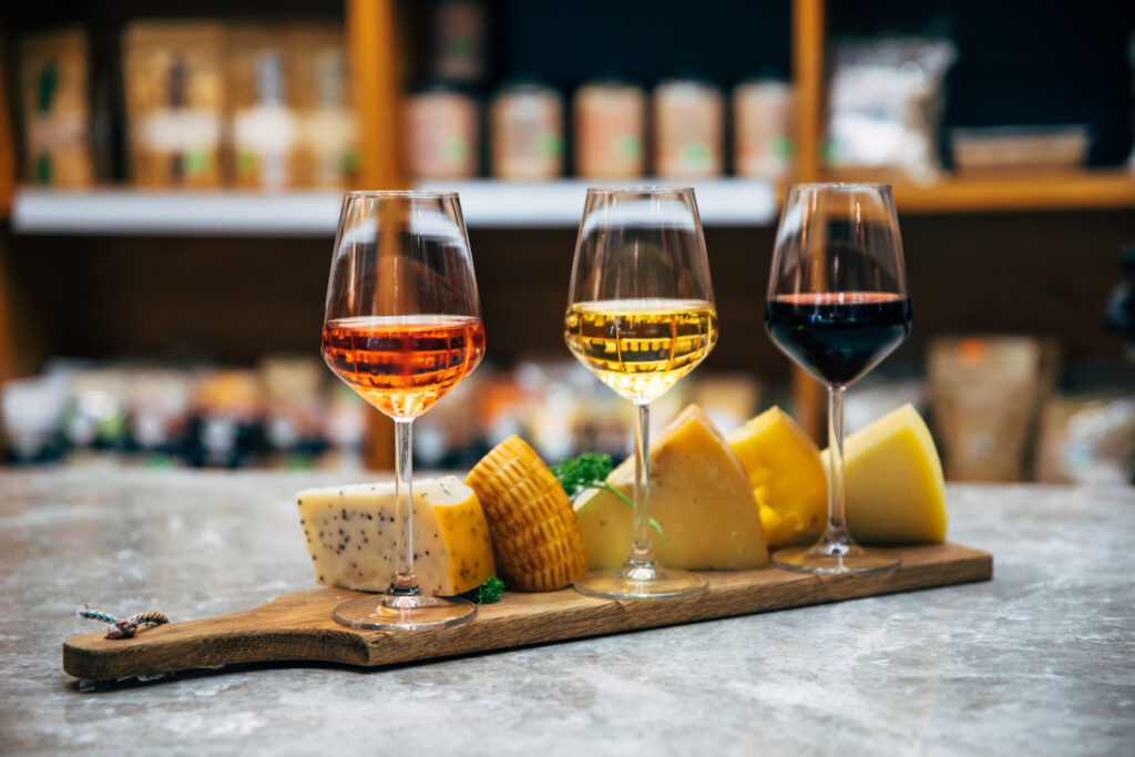 Glasses of Wine and cheese. Assortment or various type of cheese, wine glasses and bottles on the table in restaurant. Red, rose and yellow wine or champagne on the table. Winery concept image