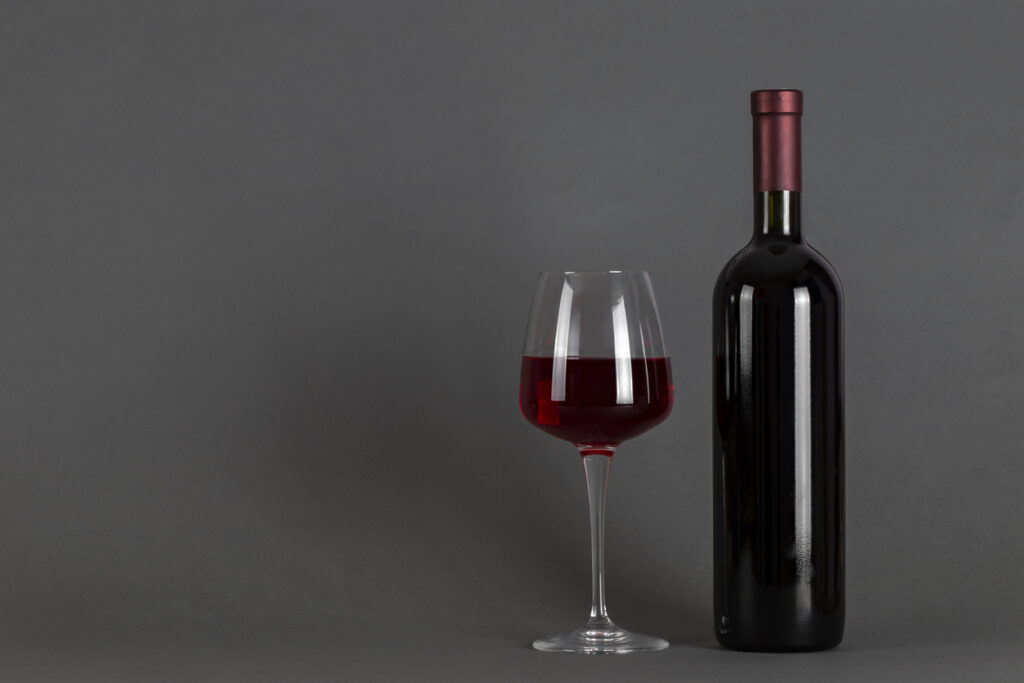 Red wine bottle and glass on a gray background. Wine drinking culture concept.