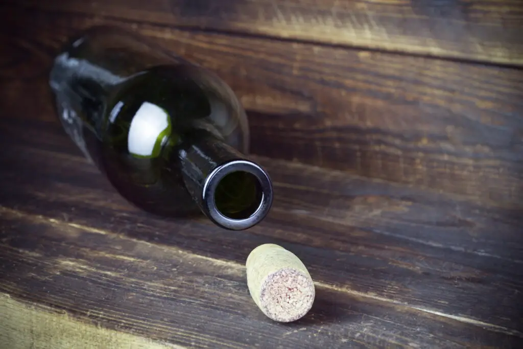 Lying empty wine bottle with cork nearby on plank wooden surface