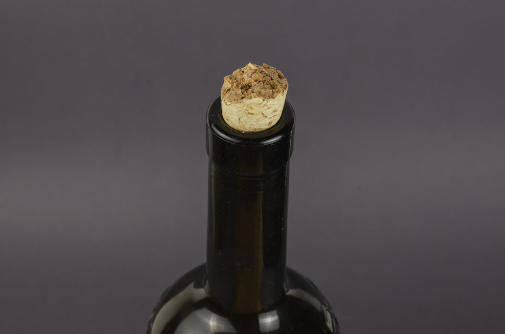 Wine bottle with broken cork on gray background.
