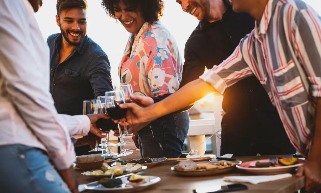 Young friends toasting with red wine at appetizer sunset time on patio house - Drink and food concept