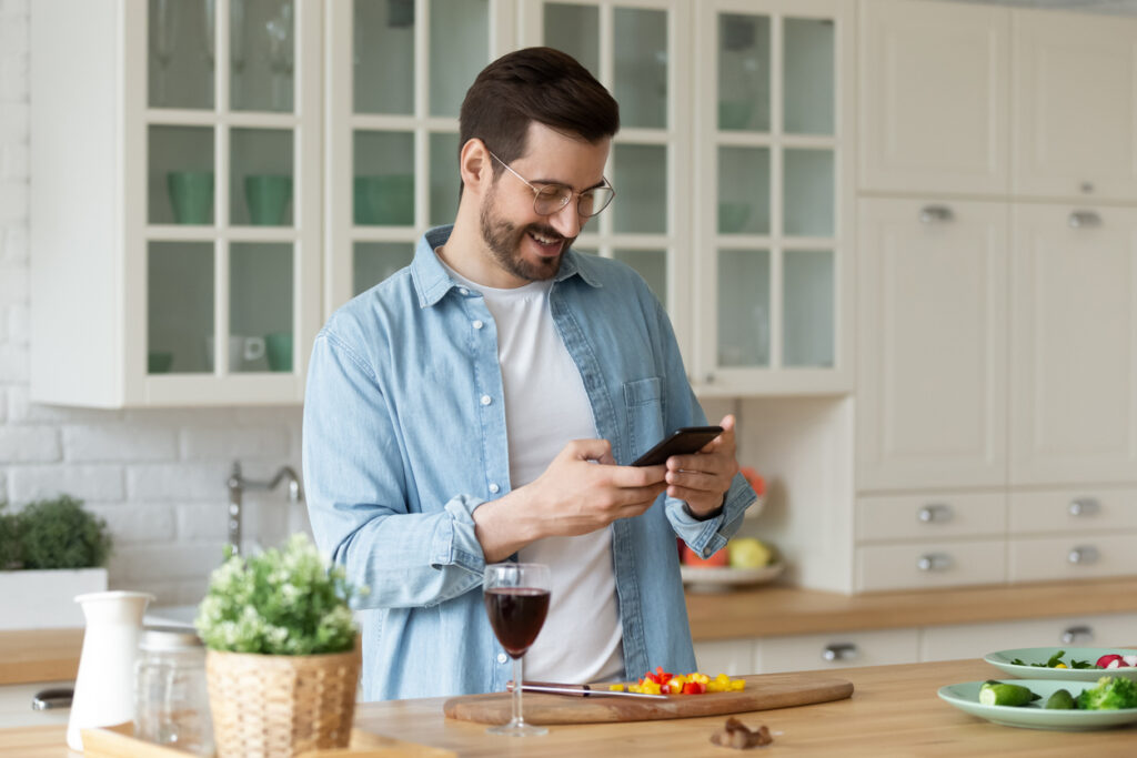 Young man read recipe on cell cooking in kitchen alone