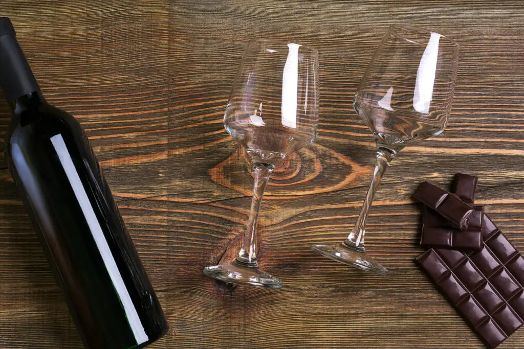 Bar of chocolate, bottle and two glasses of wine on wooden background from top view