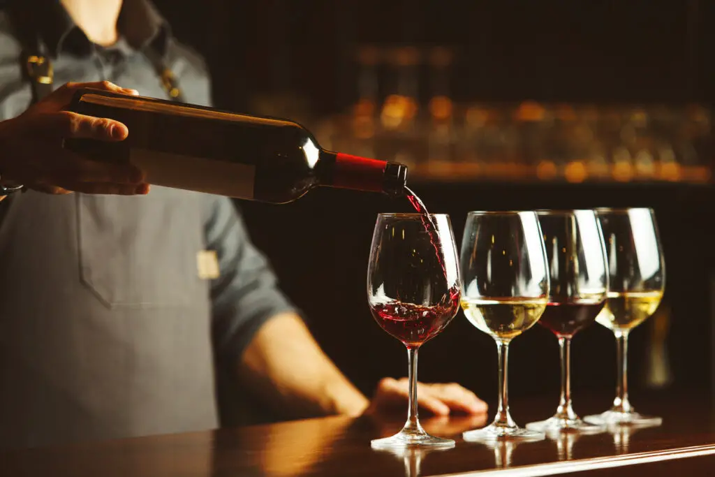 Bartender pours red wine in glasses on wooden bar counter