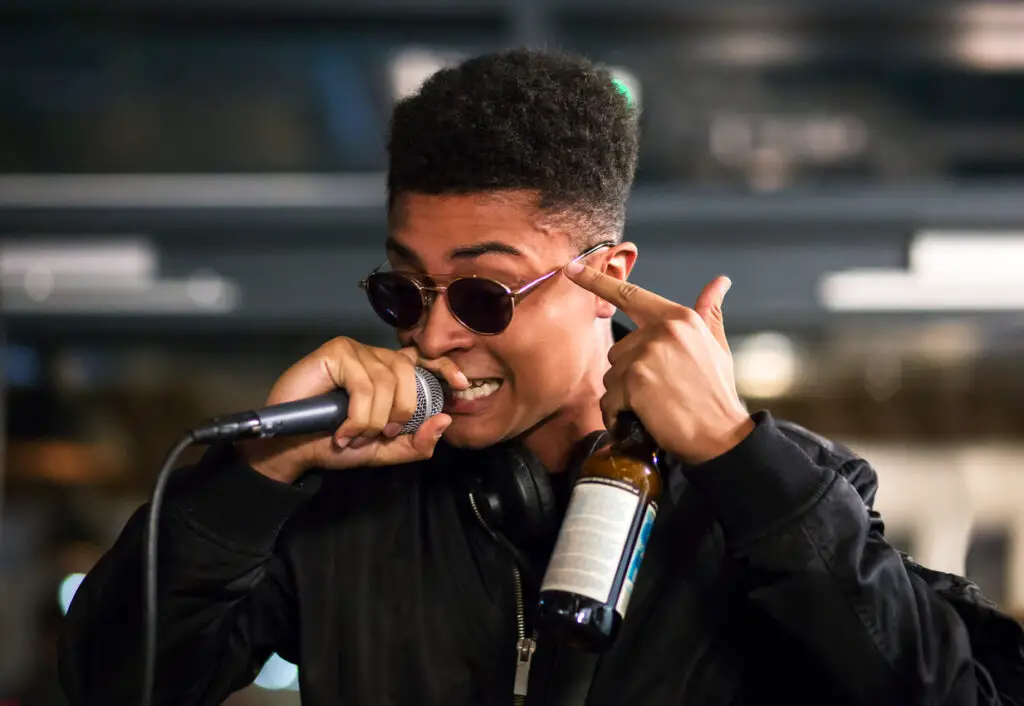 Black rapper performing with microphone, pointing to head. Bottle in hand.
