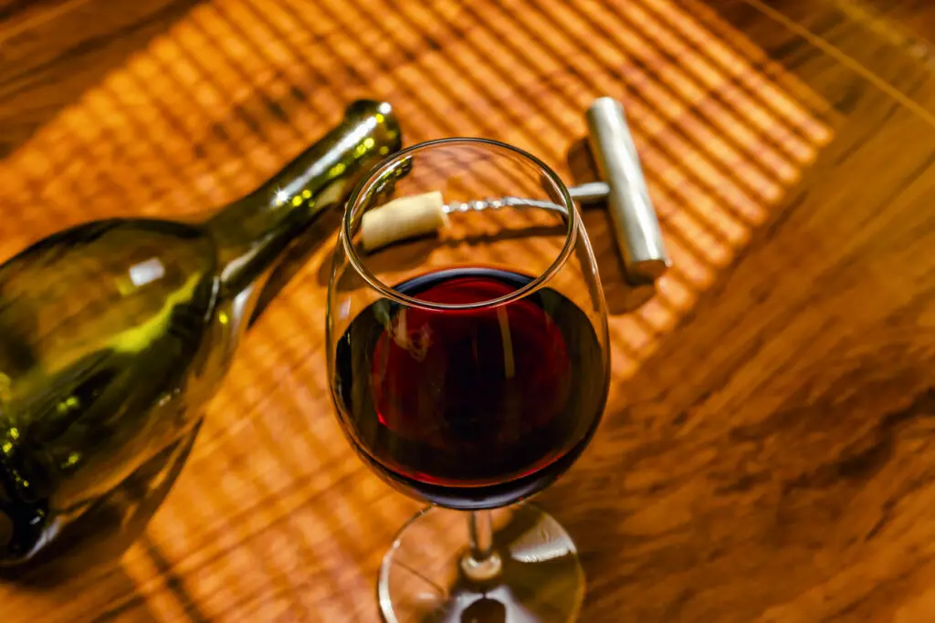 glass of red wine with bottle and corkscrew on wooden table and natural light