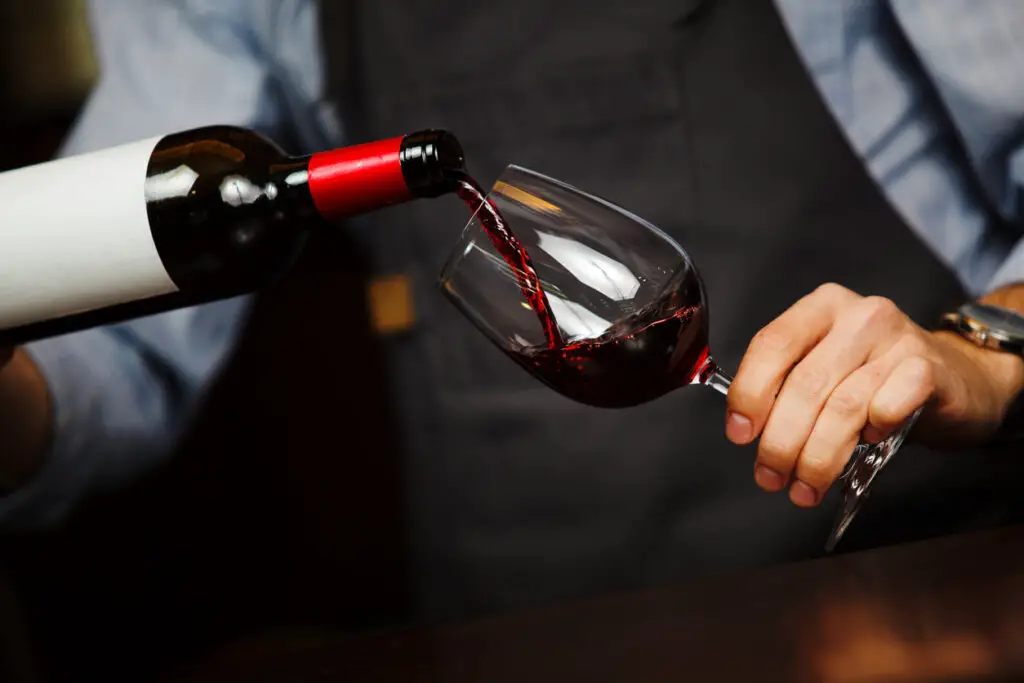 Man pouring wine into wineglass, male hand holding bottle