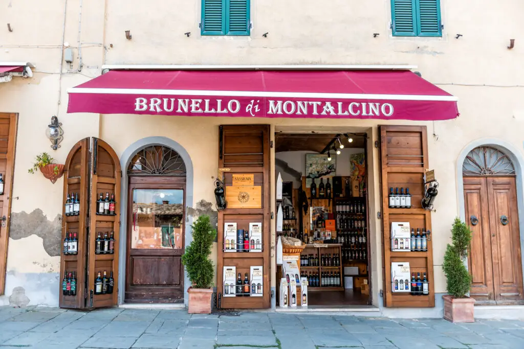 Street in town village in Tuscany during summer day and wine store with many bottles of local drink called Brunello