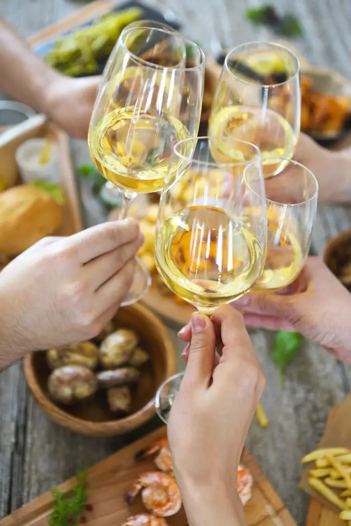 People with white wine toasting over served table with food.