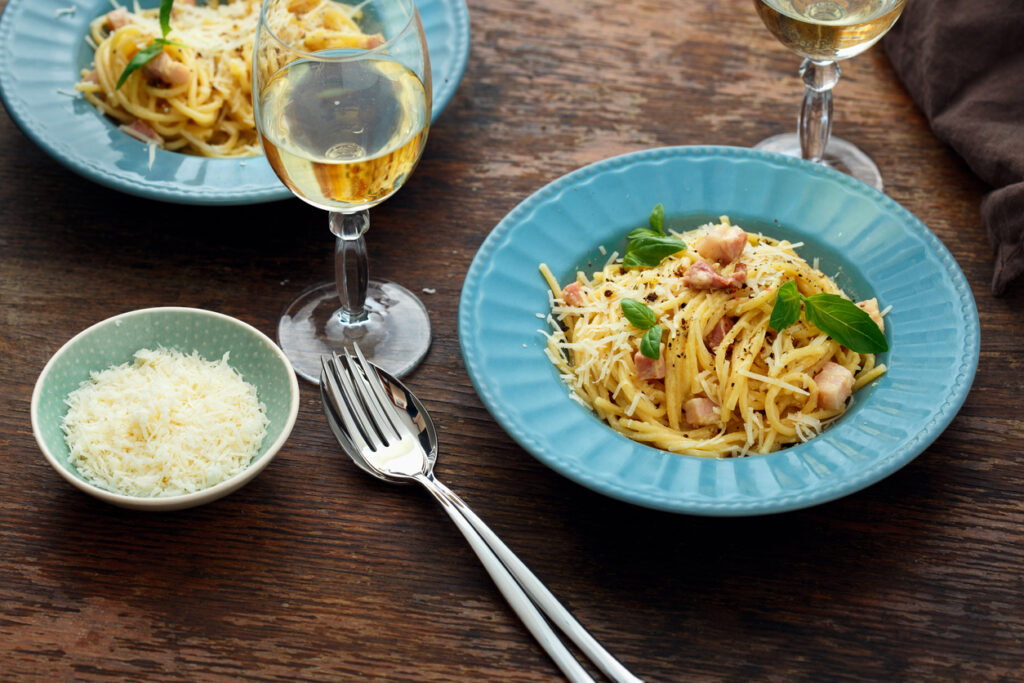 Plate pasta carbonara with glass of white wine on wooden table