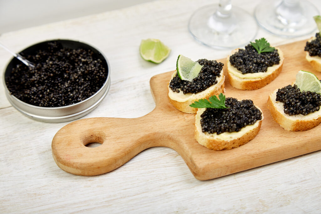 Sandwiches with black caviar. Sturgeon black caviar in wooden bowl, sandwiches and champagne on white background copy space